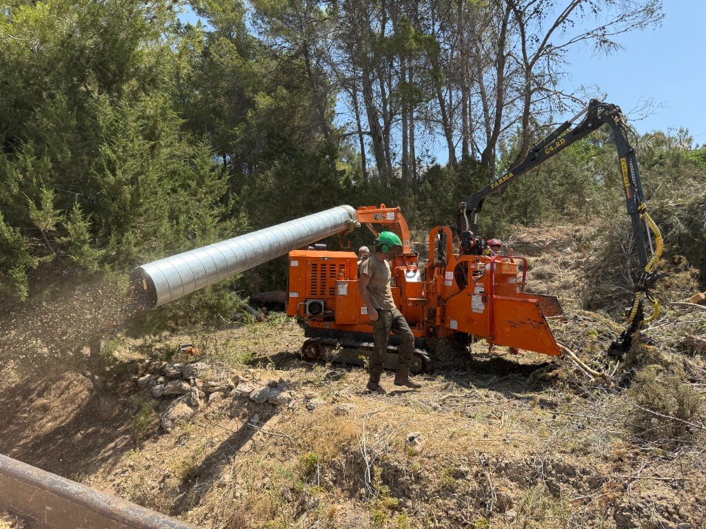 Forestry crew operating a tracked wood chipper and crane on site